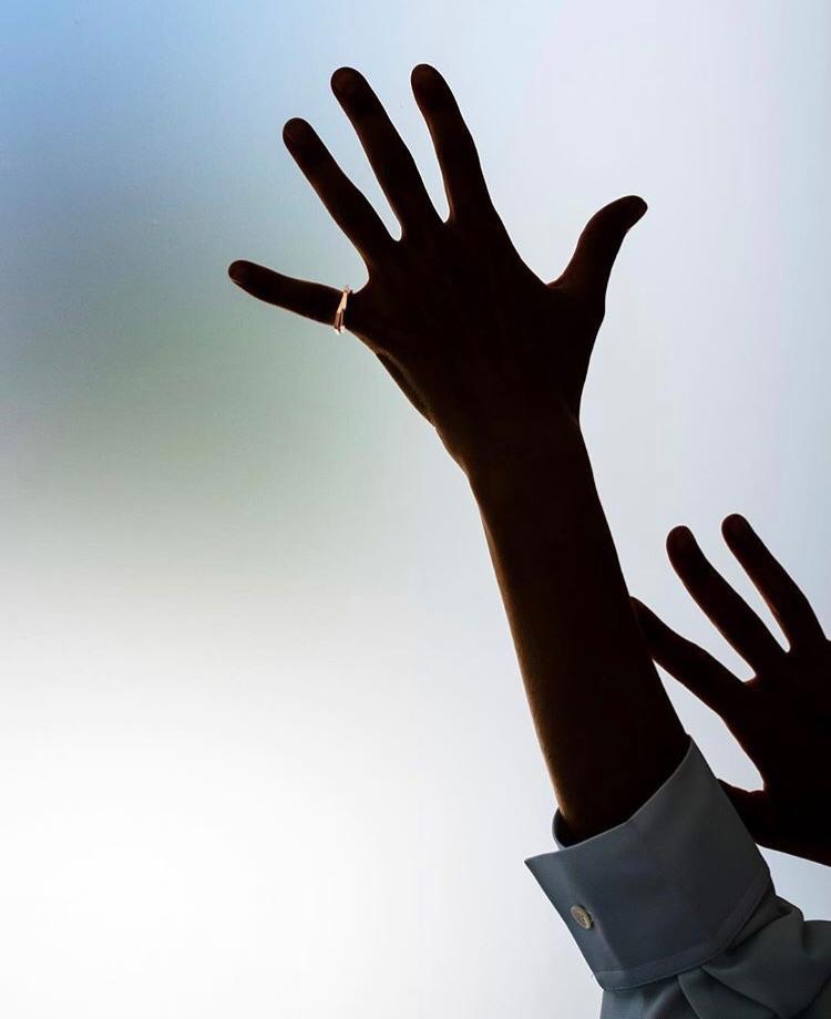 Raised hands in silhouette wearing a slim gold ring